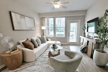 Greenville apartment for rent - A living room with a white couch, a grey armchair, a wooden side table, and a large painting on the wall.
