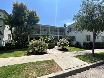 Los Angeles apartment for rent - A sunny day at a white building with trees and bushes in front.