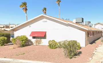 Bullhead City apartment for rent - A white building with a red awning is surrounded by palm trees.