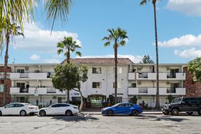 Los Angeles apartment for rent - Cars parked in front of a white apartment building with palm trees.