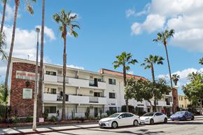 Los Angeles apartment for rent - A white car is parked in front of a white building with a red brick wall.