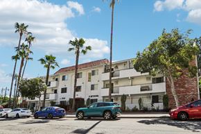 Los Angeles apartment for rent - Cars parked in front of a white apartment building with palm trees.