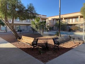 Bullhead City apartment for rent - Two wooden benches are situated in a courtyard with a tree and a building in the background.