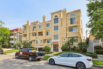 Los Angeles apartment for rent - A white car is parked in front of a building with a red truck parked behind it.
