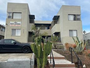 Los Angeles apartment for rent - A black car is parked in front of a building with a sign that says "NOW LEASING" and a phone number.