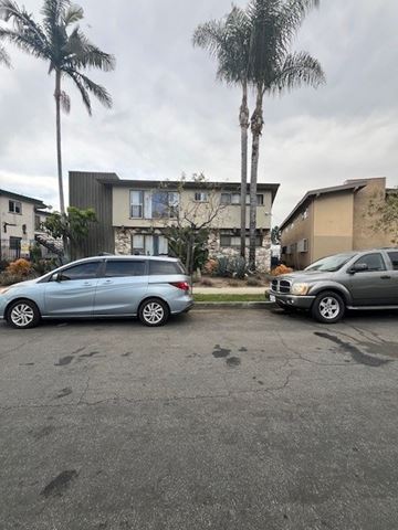 Los Angeles apartment for rent - Two cars parked in a driveway with a house and palm trees in the background.