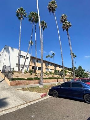 Los Angeles apartment for rent - A blue car is parked in front of a building with palm trees.