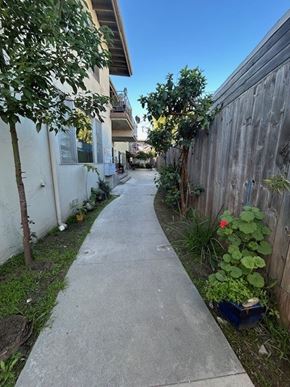 Los Angeles apartment for rent - A narrow sidewalk runs between a white building and a wooden fence.