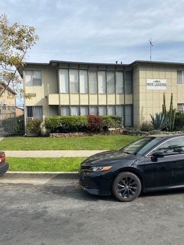 Los Angeles apartment for rent - A black car is parked in front of a building with a sign that says "NOW LEASING".