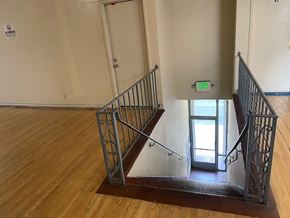 Maywood apartment for rent - A staircase with a metal railing and wooden steps leading to a door with a green exit sign above it.