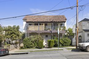 Los Angeles apartment for rent - A white house with a brown roof and a balcony is surrounded by greenery and a car is parked in front.