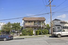 Los Angeles apartment for rent - A street view with a car parked on the side of the road and a house with a balcony in the background.