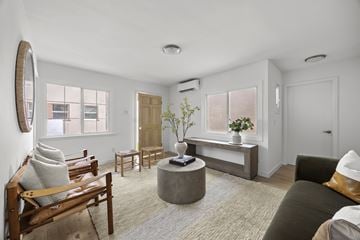 Los Angeles triplex for rent - A living room with a brown sofa, a wooden chair, a round table, and a large mirror on the wall.