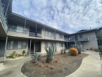 Compton apartment for rent - A concrete building with a balcony and a small garden in front.