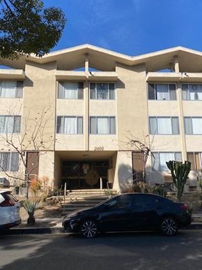 Los Angeles apartment for rent - A black car is parked in front of a tan building with a white car parked in front of it.