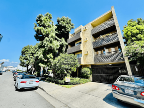 Los Angeles apartment for rent - A street view of a residential area with cars parked on the side of the road and a building with balconies in the background.