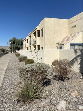 Bullhead City apartment for rent - A building with a grey facade and a blue door is surrounded by a gravel garden.
