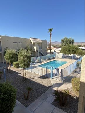 Bullhead City apartment for rent - A pool surrounded by a fence and trees in a desert landscape.