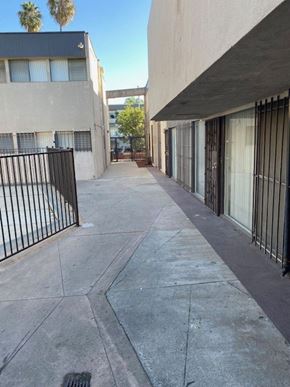 Los Angeles apartment for rent - A long concrete walkway between two buildings with a black fence on the left.