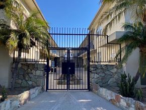 Los Angeles apartment for rent - A black gate with a stone wall and palm trees on either side.