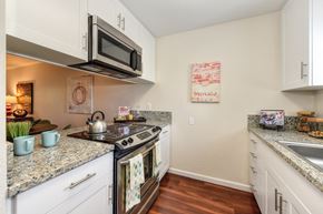 Sacramento apartment for rent - Model home kitchen with granite counter tops, white cabinets and wood flooring.  Kitchen comes with refrigerator, microwave, stove and dishwasher. at Monte Bello Apartments, Sacramento, California