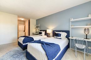 Davis apartment for rent - Model home bedroom with two beds and a desk with a chair. Stackable washer and dryer inside room at Renaissance Park Apartments, Davis, California
