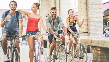 Four young adults riding bikes together.  Two people are enjoying coffee while biking.
