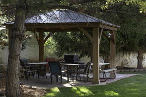 Bountiful apartment for rent - A wooden gazebo with a metal roof is surrounded by trees and has tables and chairs set up for outdoor dining.