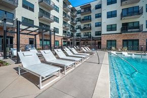 Burleson apartment for rent - A pool area with sun loungers and apartment buildings in the background.