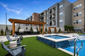 Lewisville apartment for rent - A pool with a slide and a pergola in the foreground with apartment buildings in the background.