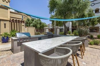 A patio with an outdoor kitchen with a grill and chairs