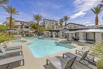 A swimming pool with chairs and umbrellas and apartments in the background