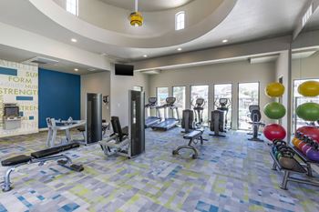 A gym with cardio equipment and weights in a large room with windows