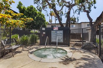 A hot tub sits in front of a black fence with a tree in the background