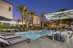 Las Vegas apartment for rent - One-Bedroom Apartments in Spring Valley, Las Vegas, NV - The Michael B Townhomes and Flats - Outdoor Pool At Twilight With Lounge Chairs, Umbrellas, Palm Trees, and Buildings With String Lights.