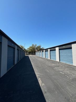 Poway apartment for rent - Outdoor storage facility with multiple units featuring blue roll-up doors and an asphalt driveway under a clear blue sky.