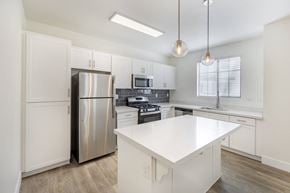 Las Vegas apartment for rent - Two-Bedroom Apartments in Spring Valley, Las Vegas, NV - The Michael B Townhomes and Flats - White Kitchen With Island, Pendant Lights, Stainless Appliances, and Faux Hardwood Floors.