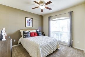 Plano apartment for rent - A bedroom with a bed, pillows, a ceiling fan, and a window with curtains.