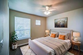Dallas apartment for rent - A bedroom with a large bed, a ceiling fan, and a window with blinds.