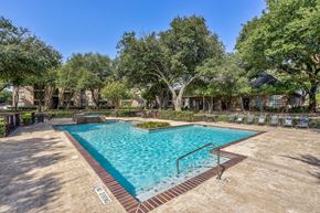 Dallas apartment for rent - A large outdoor pool surrounded by trees and a fence.