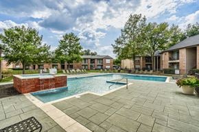 Dallas apartment for rent - A swimming pool surrounded by a brick wall and a patio area with a bench.