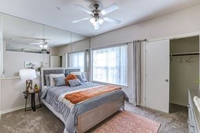 Dallas apartment for rent - A bedroom with a bed, a ceiling fan, and a mirror.