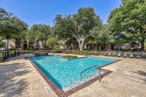 Dallas apartment for rent - A large outdoor pool surrounded by trees and a fence.