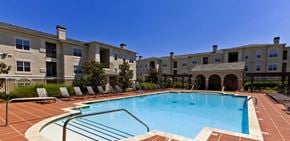 Tulsa apartment for rent - A swimming pool in front of a building with a fence and trees.