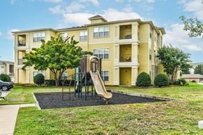 Tulsa apartment for rent - A yellow apartment building with a playground in front.