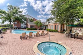 Dallas apartment for rent - A pool with a hot tub in the middle of a brick patio surrounded by chairs.