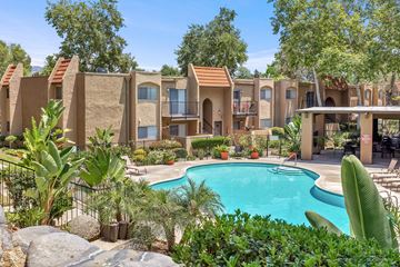 Escondido apartment for rent - A pool surrounded by green plants and trees with a building in the background.