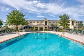 Tulsa apartment for rent - A large swimming pool in front of a building with a blue sky and clouds in the background.