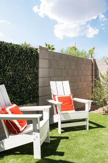 A backyard with white chairs and orange pillows