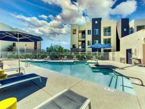 Mesa apartment for rent - Pool with buildings in the background and patio umbrella up front. Four lounge chairs line the pool.